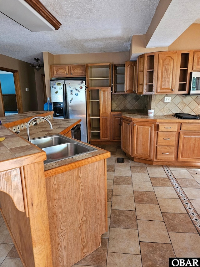 kitchen featuring brown cabinetry, a sink, stainless steel appliances, open shelves, and backsplash