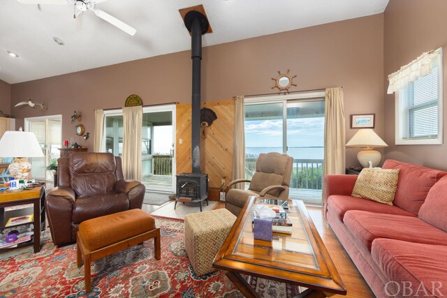 living area featuring lofted ceiling, a wood stove, and a ceiling fan