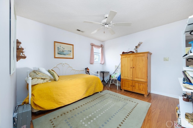 bedroom with light wood-style floors, a textured ceiling, visible vents, and a ceiling fan