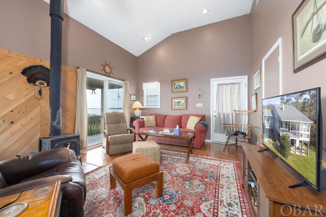 living area featuring a wood stove, light wood-style floors, and high vaulted ceiling