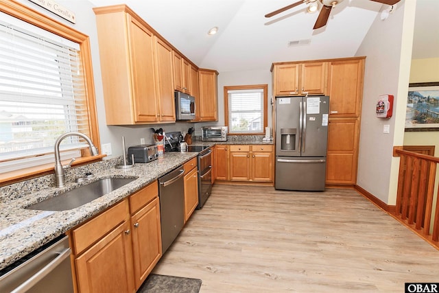 kitchen with a wealth of natural light, light stone countertops, vaulted ceiling, stainless steel appliances, and a sink