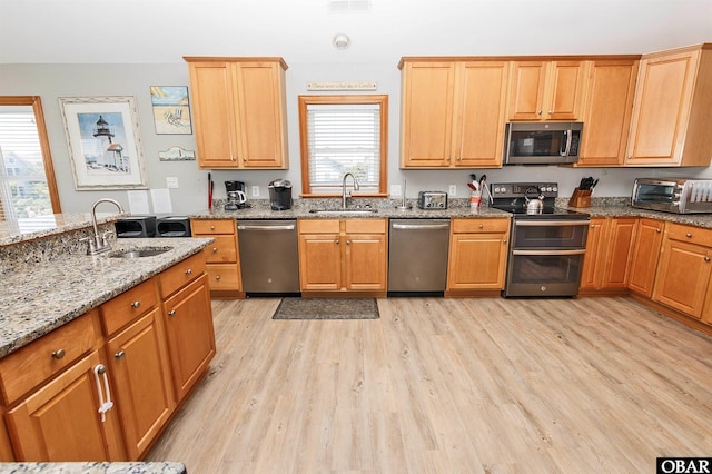 kitchen with stainless steel appliances, a toaster, a sink, and light stone countertops