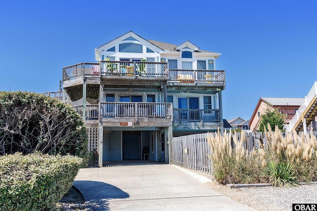 view of front of house with a carport, concrete driveway, fence, and a balcony