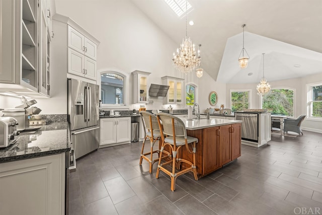 kitchen with decorative light fixtures, a center island with sink, stainless steel appliances, glass insert cabinets, and white cabinetry