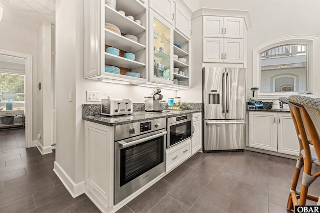 kitchen featuring white cabinets, glass insert cabinets, stainless steel appliances, and dark stone countertops