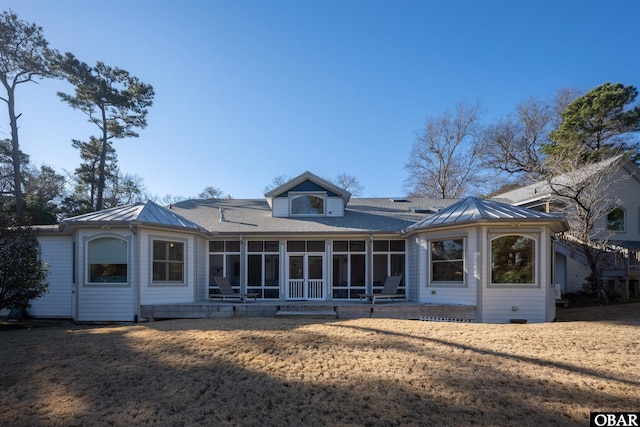 rear view of property featuring a sunroom, metal roof, a standing seam roof, and a lawn