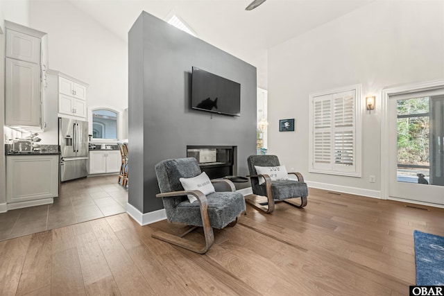 living area featuring high vaulted ceiling, a glass covered fireplace, baseboards, and light wood finished floors