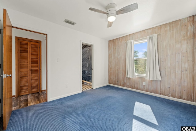 unfurnished bedroom with wood walls, visible vents, carpet flooring, and baseboards