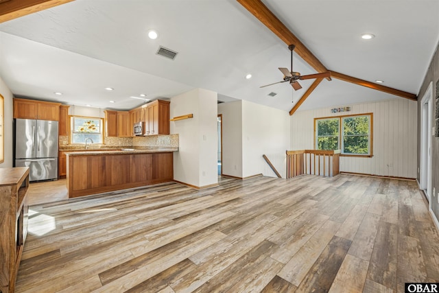 unfurnished living room with light wood finished floors, a sink, vaulted ceiling with beams, a ceiling fan, and visible vents