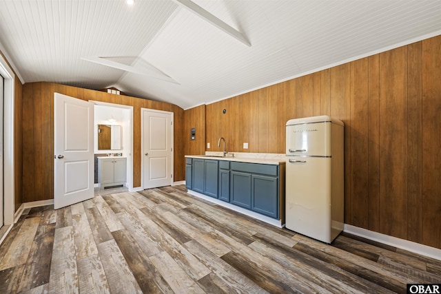 kitchen with wood finished floors, freestanding refrigerator, light countertops, wood walls, and lofted ceiling