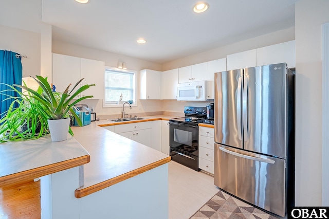 kitchen with electric range, white microwave, freestanding refrigerator, a sink, and a peninsula