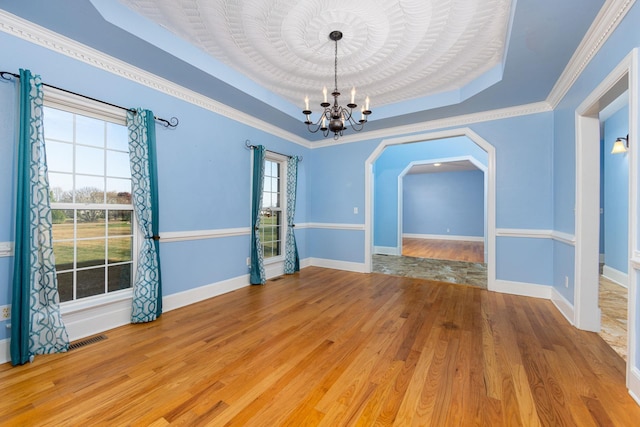 spare room featuring a chandelier, a raised ceiling, arched walkways, ornamental molding, and wood finished floors