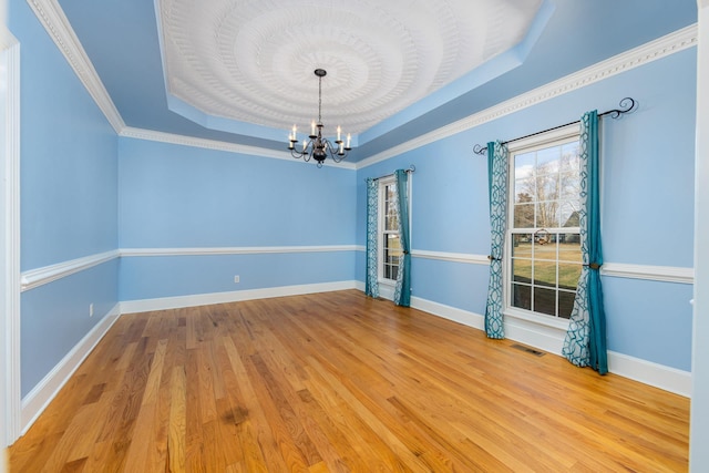 spare room with visible vents, a notable chandelier, a raised ceiling, and light wood-type flooring