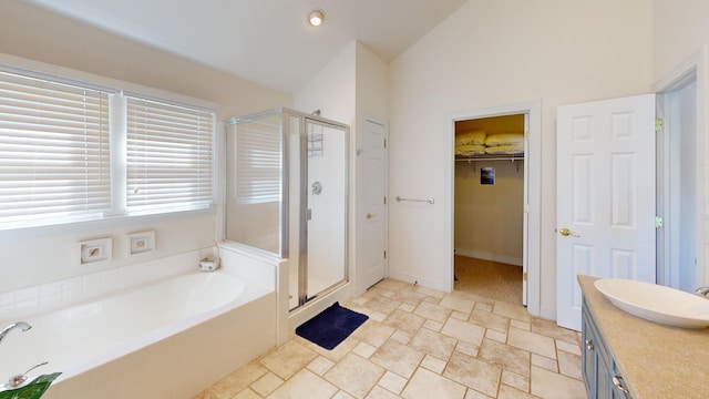 bathroom featuring a garden tub, vaulted ceiling, a walk in closet, vanity, and a shower stall