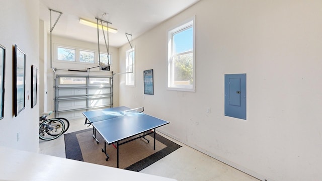 recreation room featuring a garage, a healthy amount of sunlight, electric panel, and concrete floors