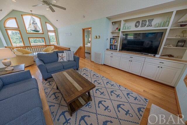 living area with built in features, visible vents, light wood-style floors, a ceiling fan, and high vaulted ceiling