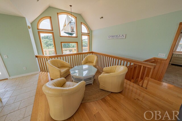 living area featuring a wainscoted wall, visible vents, an upstairs landing, high vaulted ceiling, and light wood-type flooring