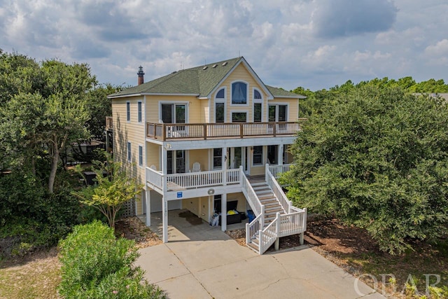 back of house with a chimney, a porch, concrete driveway, a garage, and stairs