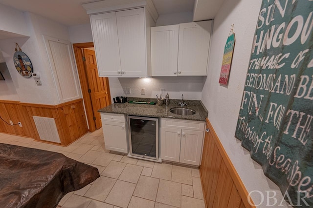 kitchen featuring beverage cooler, a wainscoted wall, a sink, visible vents, and white cabinets