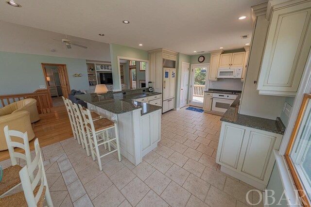 kitchen featuring white appliances, a breakfast bar, open floor plan, dark stone countertops, and a peninsula