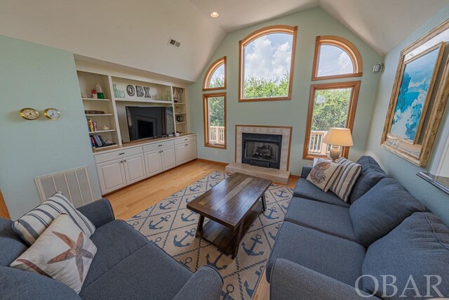 living room featuring high vaulted ceiling, light wood finished floors, a premium fireplace, and visible vents