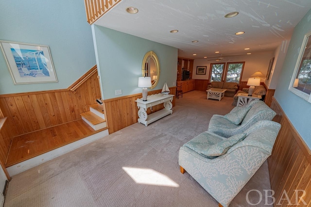 living area featuring light carpet, a wainscoted wall, wood walls, and stairway