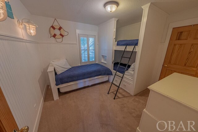 bedroom with light carpet, a textured ceiling, and a wainscoted wall