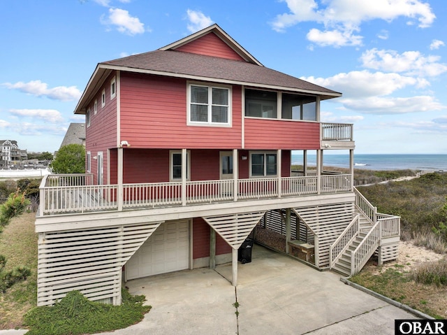 beach home featuring stairs, a water view, concrete driveway, roof with shingles, and a garage
