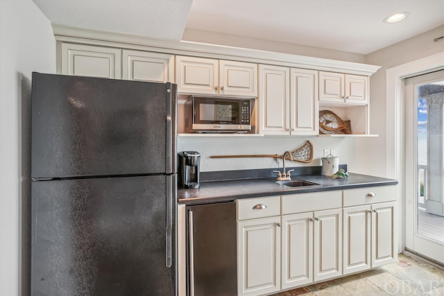 kitchen featuring open shelves, dark countertops, freestanding refrigerator, a sink, and stainless steel refrigerator