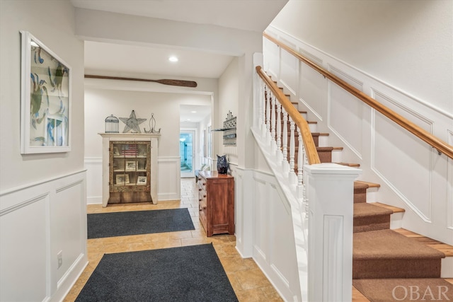 stairs with recessed lighting, wainscoting, and a decorative wall