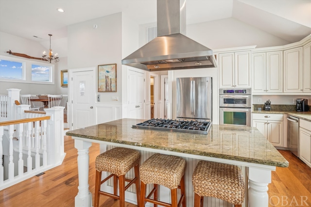 kitchen with island range hood, a center island, light stone countertops, stainless steel appliances, and light wood-type flooring