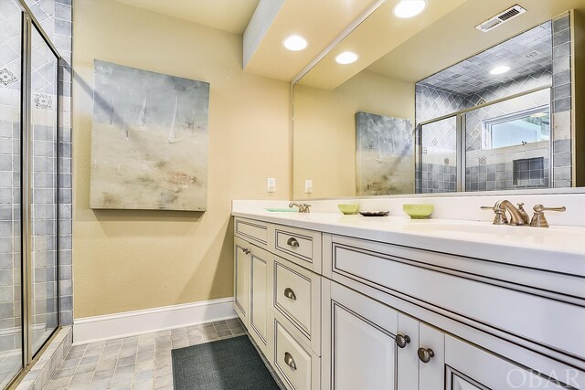 full bath with double vanity, baseboards, visible vents, a shower stall, and a sink