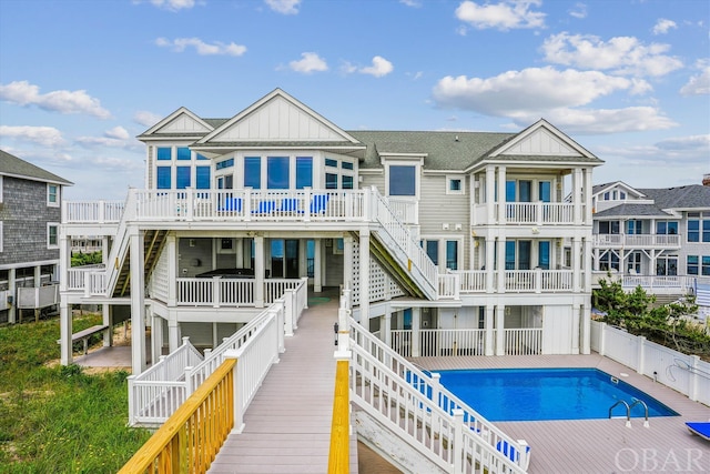 rear view of property with board and batten siding, stairs, fence, and a fenced in pool