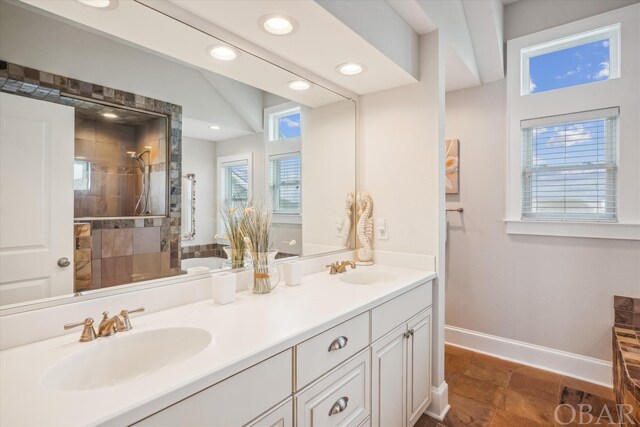 bathroom with double vanity, a sink, baseboards, and a walk in shower