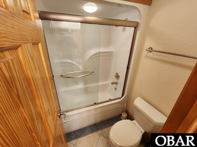 full bathroom featuring toilet, shower / bath combination with glass door, a textured wall, and tile patterned floors