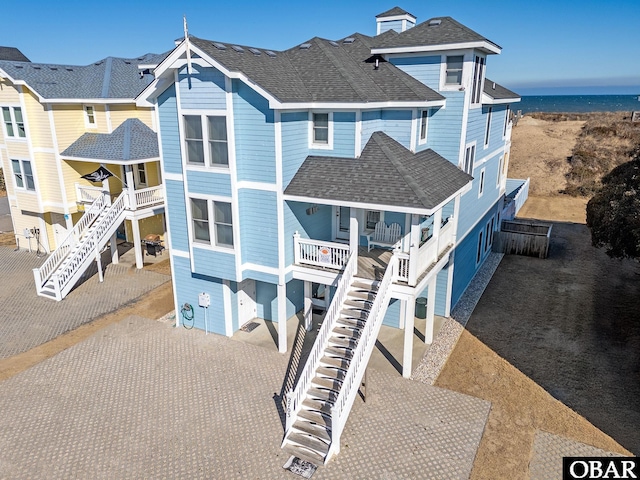 view of front of house featuring decorative driveway, roof with shingles, a water view, and stairway