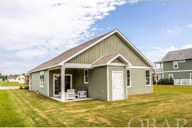 back of house with a patio area, roof with shingles, board and batten siding, and a yard