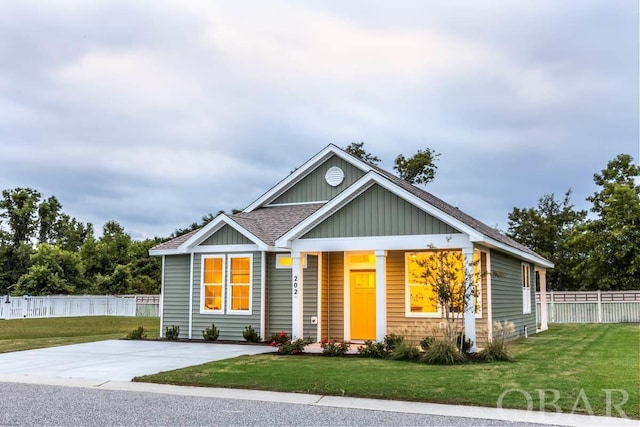 view of front facade featuring roof with shingles, board and batten siding, a front yard, and fence