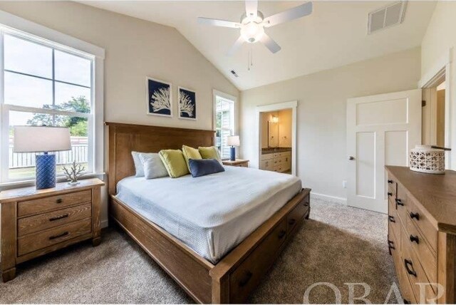 bedroom with ensuite bathroom, a ceiling fan, visible vents, vaulted ceiling, and dark colored carpet