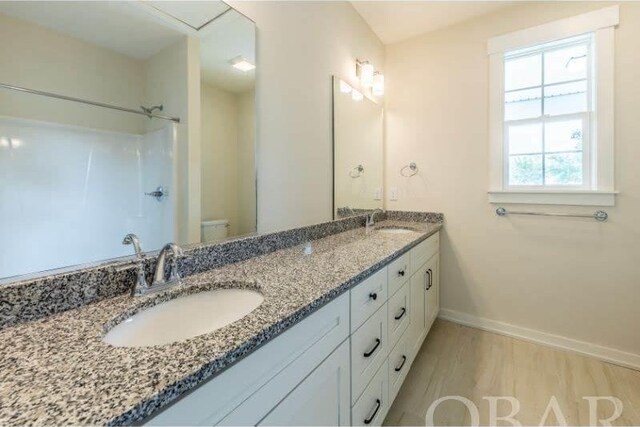 bathroom featuring toilet, double vanity, baseboards, and a sink