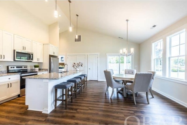 kitchen with a kitchen island with sink, stainless steel appliances, white cabinetry, a kitchen bar, and pendant lighting