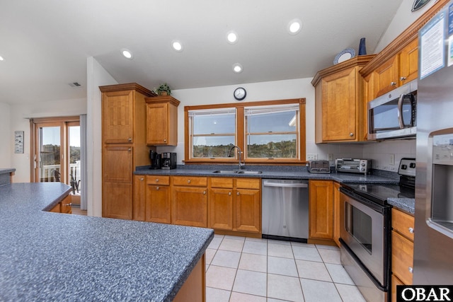 kitchen with dark countertops, appliances with stainless steel finishes, brown cabinets, and a sink