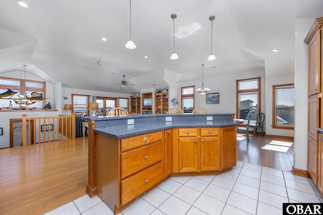 kitchen featuring light tile patterned floors, an island with sink, brown cabinets, and pendant lighting