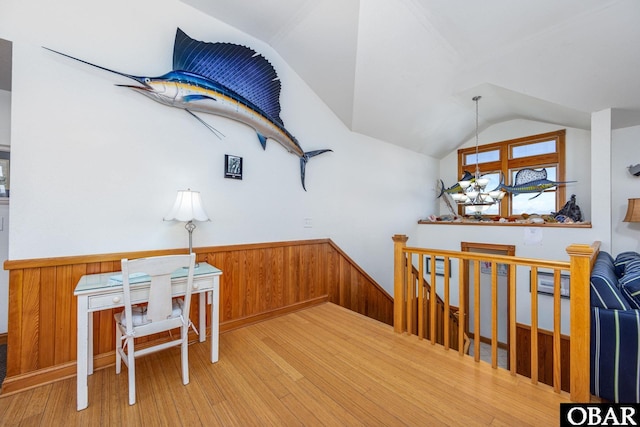 dining room with wooden walls, a wainscoted wall, a notable chandelier, light wood-style floors, and vaulted ceiling