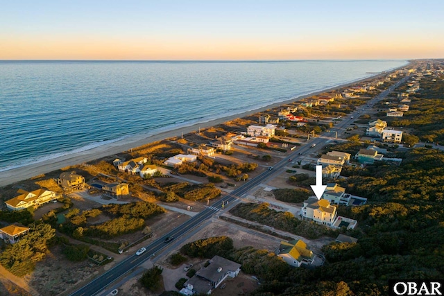 aerial view at dusk featuring a water view and a beach view