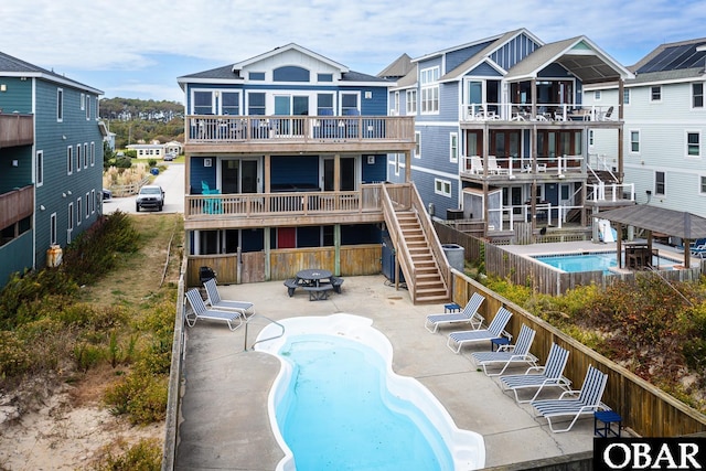 rear view of house with an outdoor fire pit, a community pool, fence, stairs, and a patio area