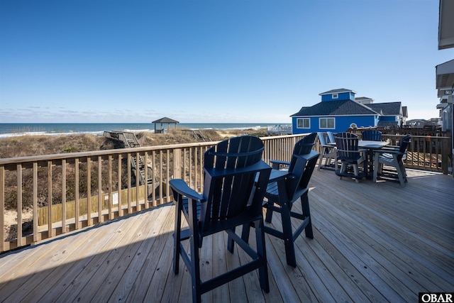 wooden terrace with a water view, a view of the beach, and outdoor dining space