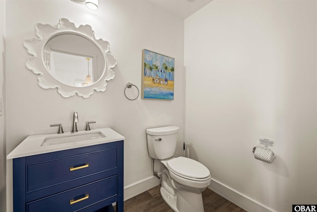 half bathroom featuring wood finished floors, vanity, toilet, and baseboards