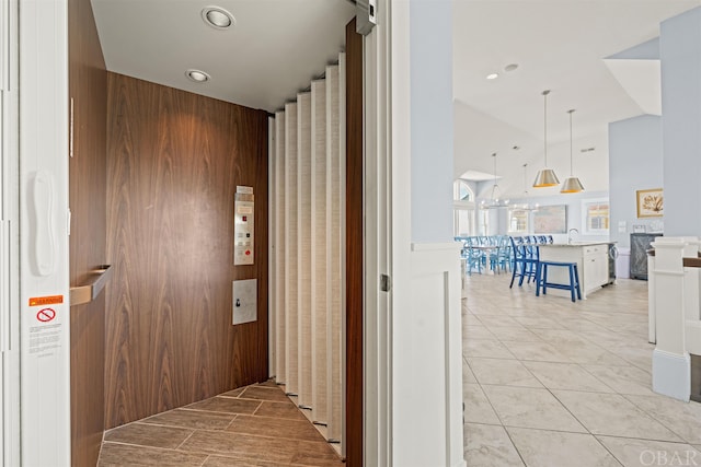 corridor with light tile patterned floors, lofted ceiling, elevator, a sink, and recessed lighting