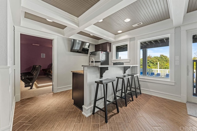 kitchen featuring a breakfast bar area, visible vents, dark brown cabinets, ornamental molding, and freestanding refrigerator